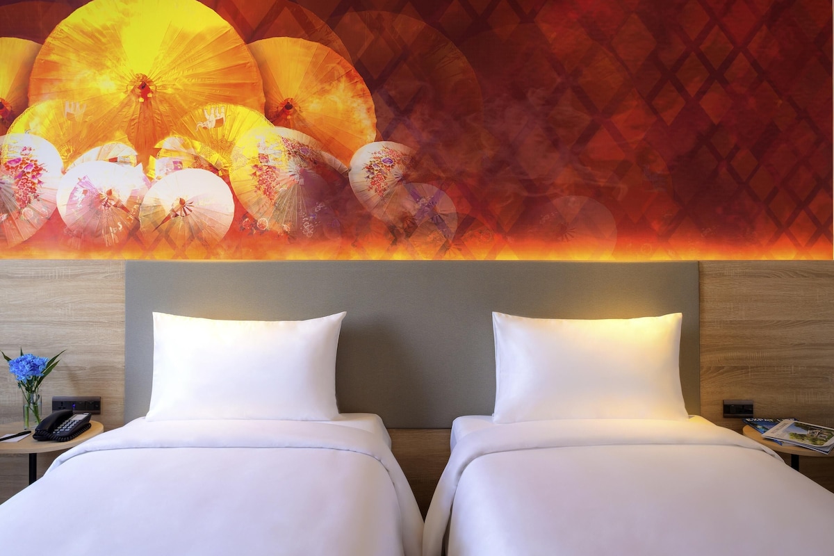 A hotel room with a large bed, two pillows, a bedside table with a phone, and a wall with a decorative mural.