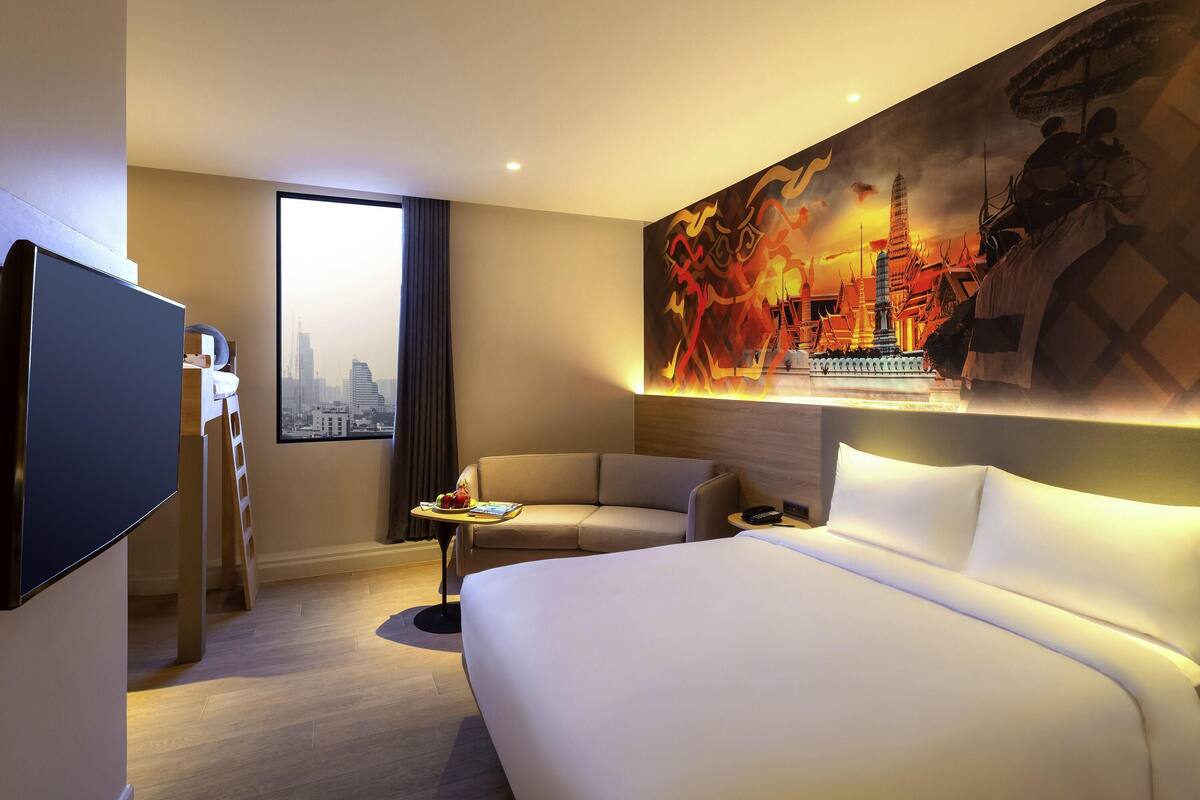 Une chambre d’hôtel avec un lit, un canapé, une télévision, un tableau et une fenêtre donnant sur le paysage urbain.