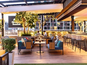 An outdoor seating area with modern furniture, a large tree, and a view of the cityscape. - ibis Styles Bangkok Ratchada (Bangkok)