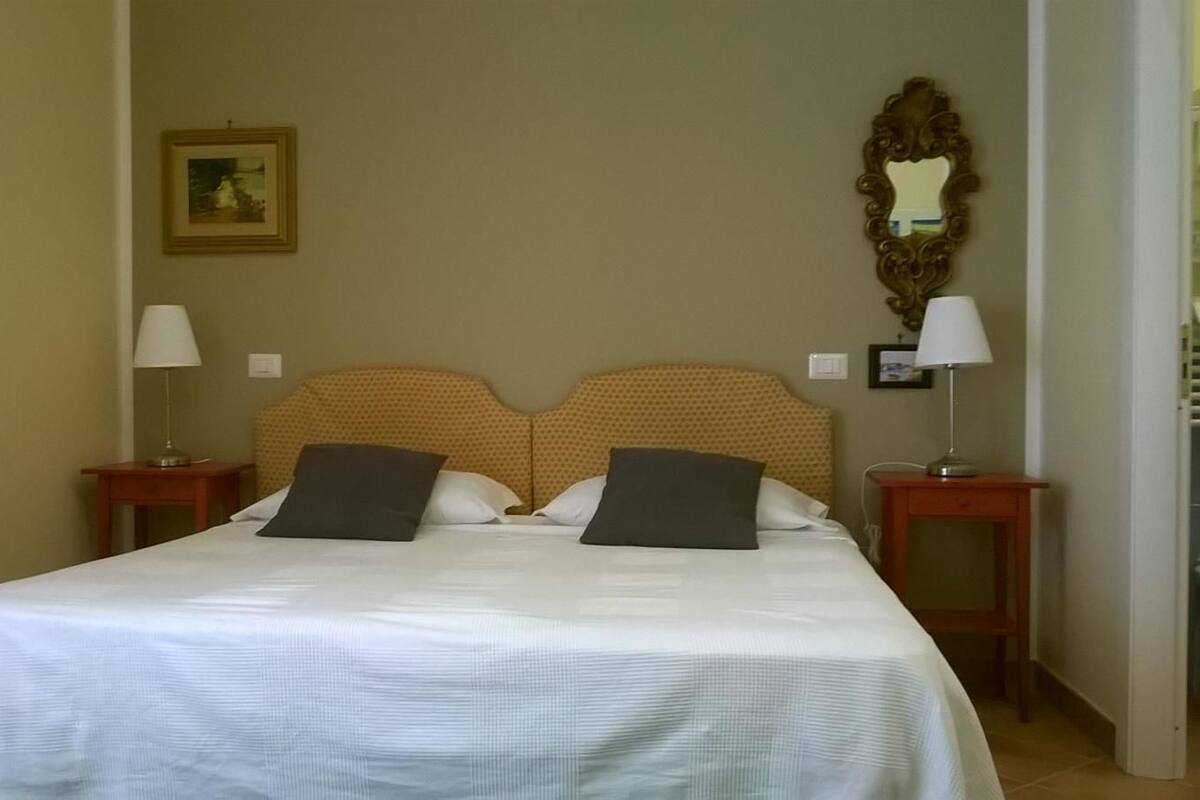 Una cama bien hecha con cabecera, dos mesitas de noche con lámparas y un cuadro en la pared.