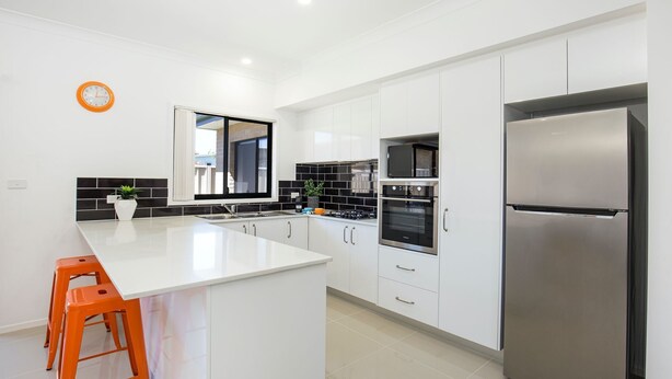 A modern kitchen with white cabinets, a stainless steel refrigerator, a double oven, and a large island with orange stools. - Villa Mare - 4 Mins to Beach (Culburra Beach)