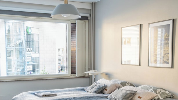 A bedroom with a large bed, a bedside table, a floor lamp, and a window with blinds.