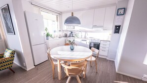 A modern kitchen with white cabinets, a round wooden table, and a pendant light.