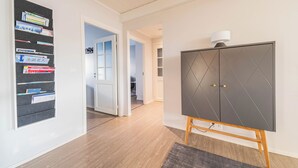 A modern interior with a wooden floor, a grey cabinet with a lamp, and a wall-mounted shelf with books.