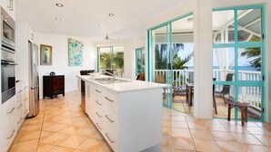Uma cozinha moderna com ilha central, armários brancos e uma grande janela com vista para uma varanda.