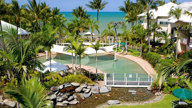 Um resort com piscina, cercado por palmeiras e vista para o oceano.