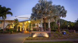 Entrada do Coral Sands Beachfront Resort, com uma palmeira e uma placa.