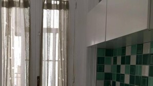 Una cocina con un lavamanos, salpicadero a cuadros verdes y cortinas de tela ligera.
