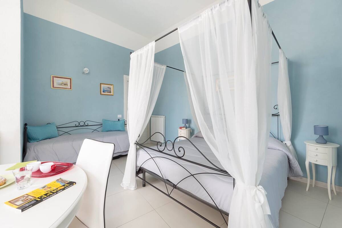 Un dormitorio con cama con dosel, una mesita de noche con lámpara y una pequeña mesa con cosas para el desayuno.