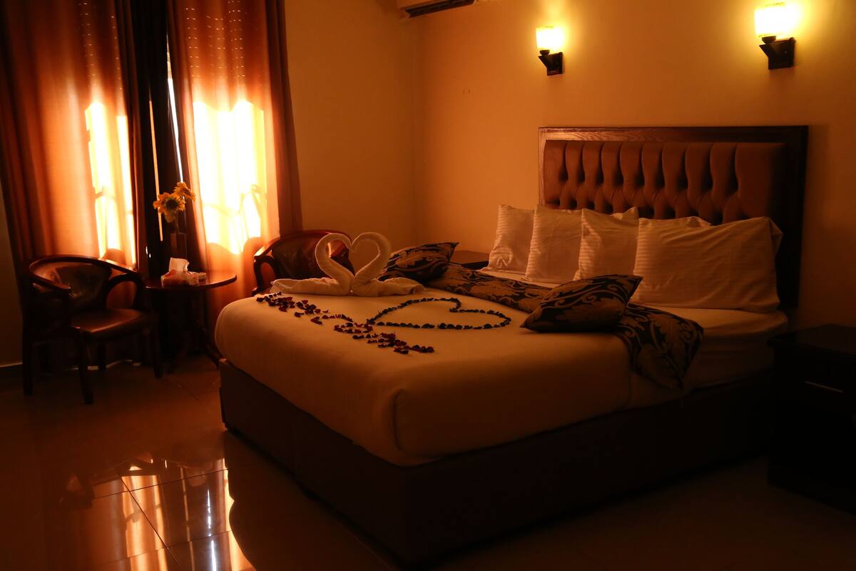 A hotel room with a large bed, a bedside table, a chair, and a lamp.