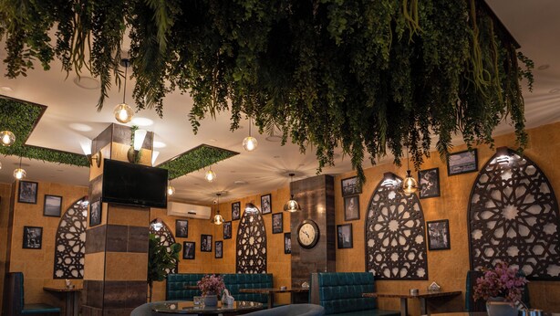 Un restaurant doté d’un plancher en bois, de sièges rembourrés en tissu bleu, de plantes suspendues et d’œuvres d’art encadrées qui ornent les murs.