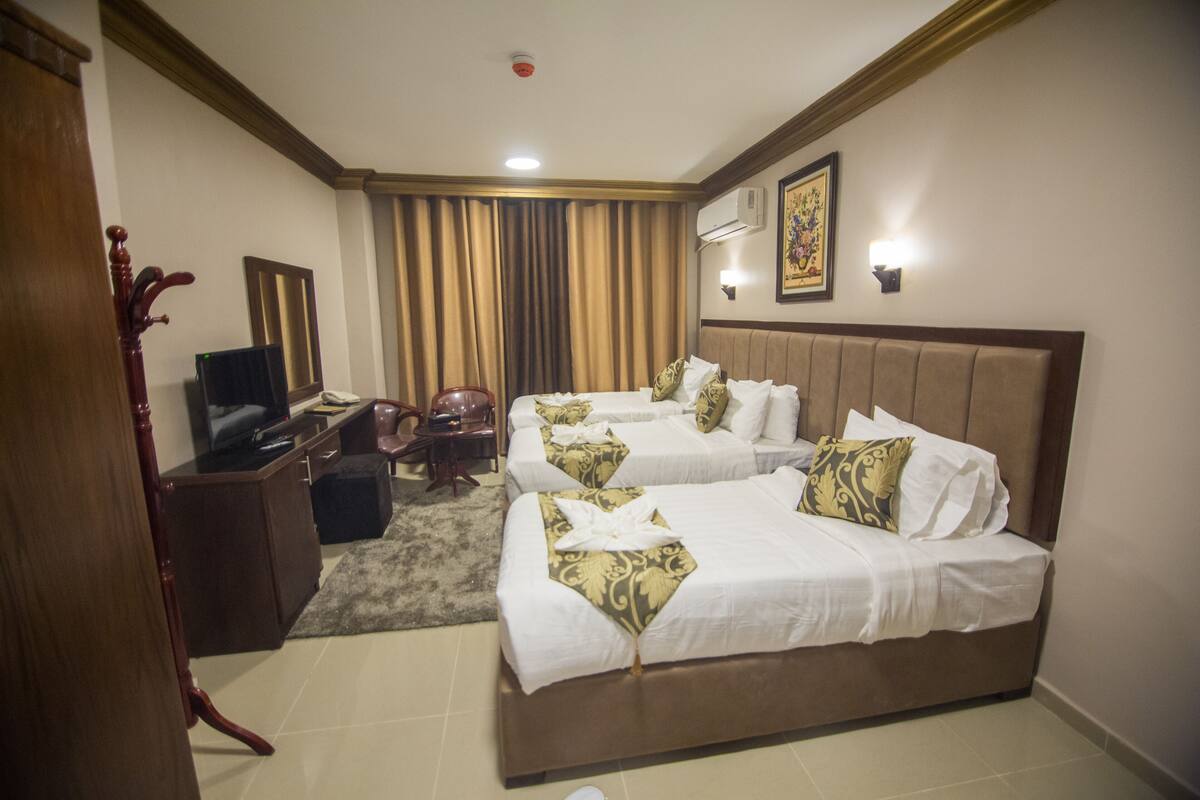 A hotel room with two beds, a desk with a computer, a chair, and a television.