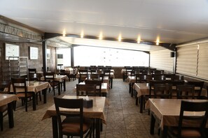 A spacious indoor dining area with multiple tables and chairs, a tiled floor, and a large window providing natural light. - Grape Village Hotel (Amman)