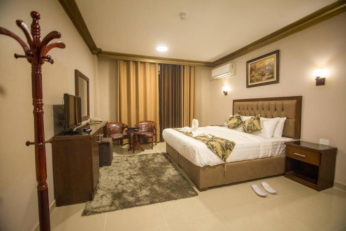 A hotel room with a bed, bedside table, desk, chair, and a coat rack.