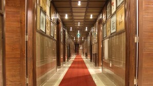 Un long couloir étroit, recouvert d’un tapis rouge, avec des lambris en bois sur les murs et des tableaux encadrés sur la partie supérieure.