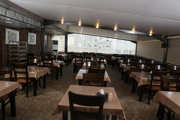 Un restaurante con varias mesas y sillas, una pared con diseño y piso de baldosas.