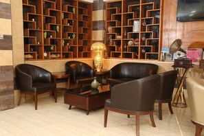 A lobby with a seating area, wooden shelving with various items, and a television. - Grape Village Hotel (Amman)