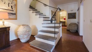 Un escalier avec des marches en pierre et une rampe en fer forgé, menant à un palier où se trouvent une lampe rouge et un tableau encadré.