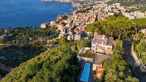 Un pueblo costero con una piscina destacada, edificios residenciales densos y montañas al fondo.