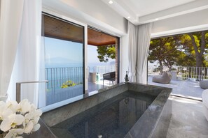 A modern interior with a large window, a marble bathtub, and a balcony with outdoor furniture. - AMORE RENTALS -Villa Giada with Swimming Pool, Garden, Sea View and Parking (Sorrento)