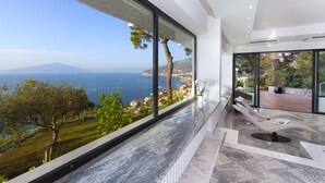 Un interior moderno con un gran ventanal con vistas al mar, suelo de mármol y una silla de estar original.