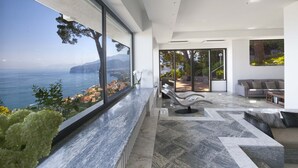 Un interior moderno con un amplio ventanal con vistas al mar, una zona de estar con una silla original y un sofá.