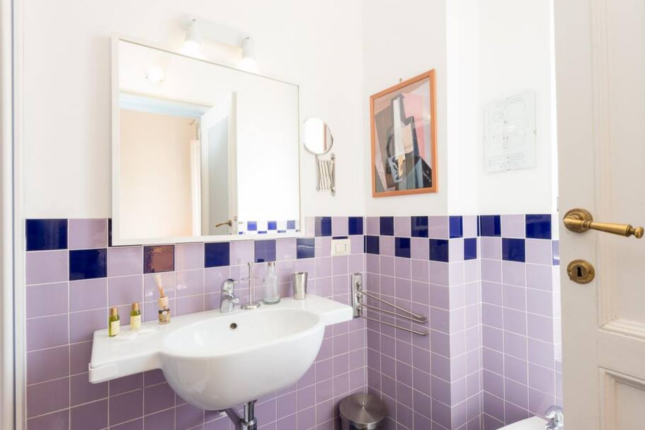 A bathroom with a white sink, a mirror, a framed picture on the wall, and a door with a brass handle.