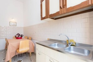 A kitchenette with a double sink, wooden cabinets, a dining table with chairs, and a tiled backsplash.