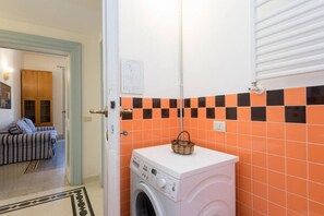 Un cuarto de lavado con lavadora, un cesto encima y pared de azulejos.