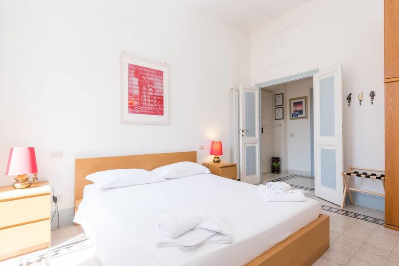 A bedroom with a bed, bedside tables, a lamp, a door, and a wall-mounted picture.