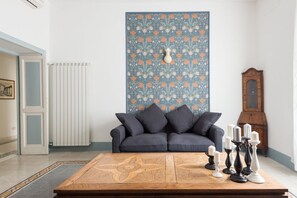 Sala de estar com parede estampada em azul, sofá escuro, mesa de centro de madeira e um relógio de pêndulo.