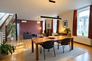 Un salon moderne comprenant un coin repas, un escalier et de grandes fenêtres avec des rideaux.