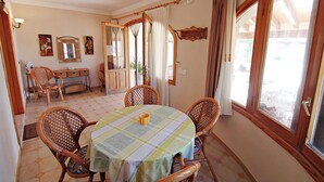 A dining area with a table set for four, surrounded by wicker chairs, a wooden buffet, and a large window with curtains. - El Ventorrillo - holiday home with stunning views and private pool in Benissa (Benissa)