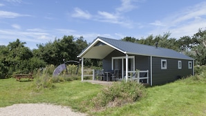 A small, single-story cabin with a covered porch, a picnic table, and a bicycle in the foreground. - Strand 49 Camping & Glamping (Sint Maartensbrug)