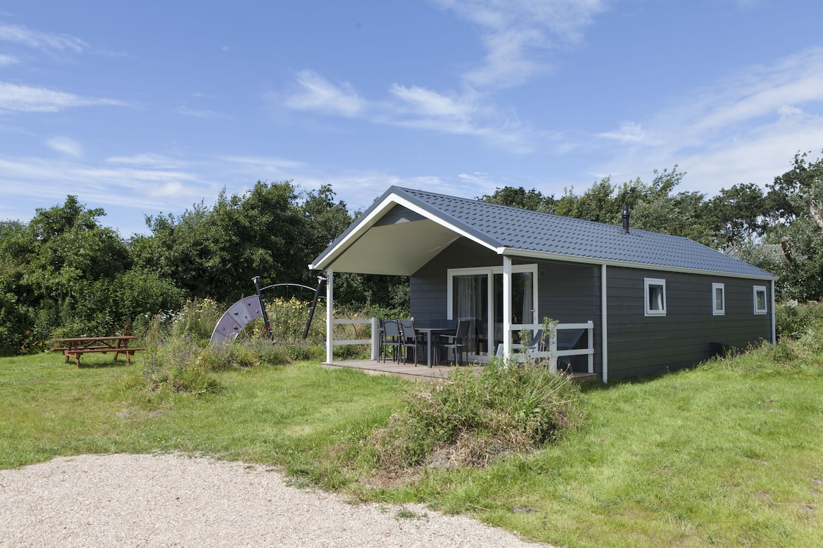 A small, single-story cabin with a covered porch, a picnic table, and a bicycle in the foreground.