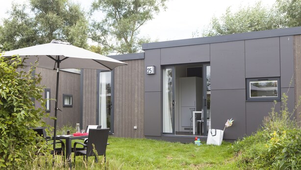 A modern building with a number 25 sign, a covered outdoor seating area, and a grassy yard. - Strand 49 Camping & Glamping (Sint Maartensbrug)