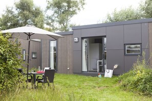 A modern building with a number 25 sign, a covered outdoor seating area, and a grassy yard. - Strand 49 Camping & Glamping (Sint Maartensbrug)
