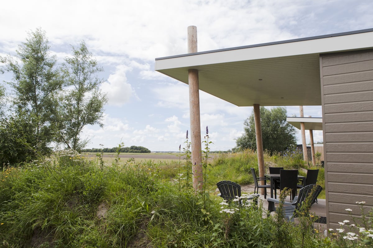 An outdoor patio with a table and chairs, surrounded by greenery and a view of a field.