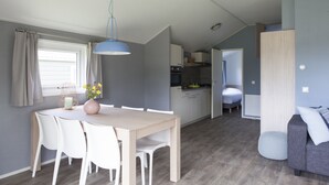 A modern, compact living space with a dining area, kitchenette, and a sleeping area. - Strand 49 Camping & Glamping (Sint Maartensbrug)