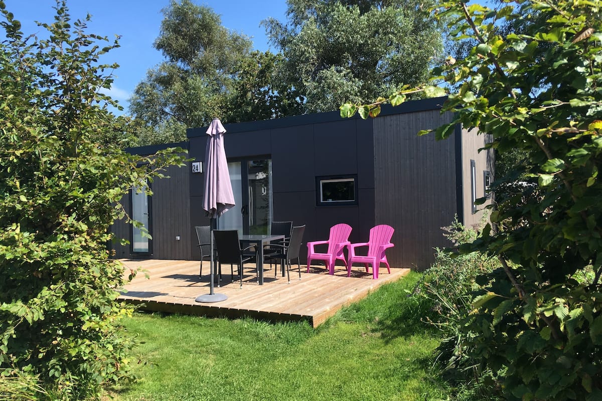 A modern outdoor patio with a wooden deck, a table with chairs, and a pink umbrella.