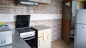 A kitchen with a gas stove, oven, and a microwave. There is a wooden door and a refrigerator. - Waterworld Apartments (Ibadan)