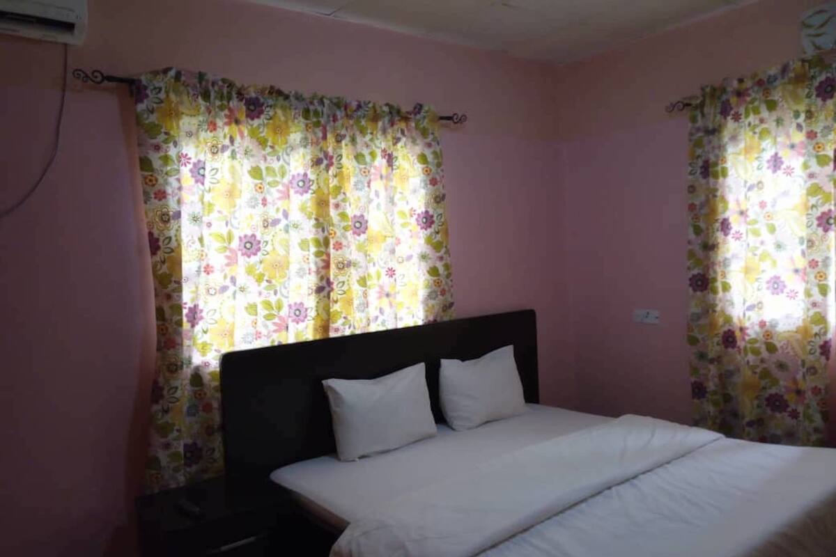 A bedroom with a bed, curtains, and an air conditioning unit.