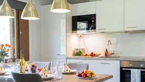 Une cuisine moderne avec des meubles blancs, une table à manger en bois et des luminaires suspendus.