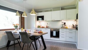 Une cuisine moderne avec des meubles blancs, une table à manger avec des chaises et des luminaires suspendus.