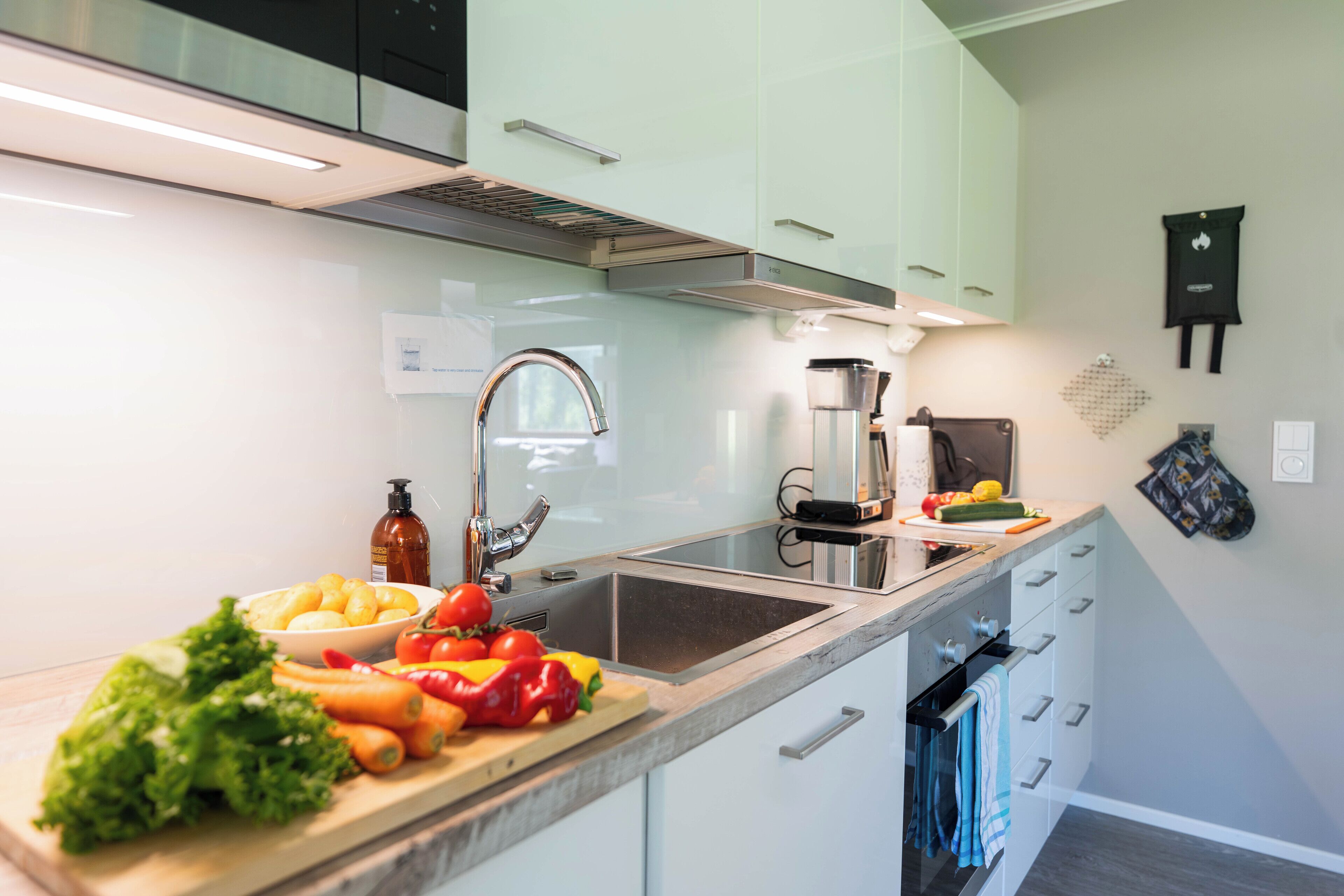 A modern kitchen with white cabinets, a stainless steel sink, and a variety of fresh vegetables on the counter.
