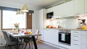 Une cuisine moderne avec des meubles blancs, un four encastré et un four à micro-ondes. On y trouve une table à manger avec des chaises et un vase rempli de fleurs.