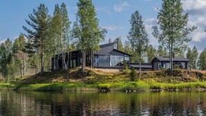 Een modern huis met grote glasramen, gelegen aan een meer met omliggende bomen.