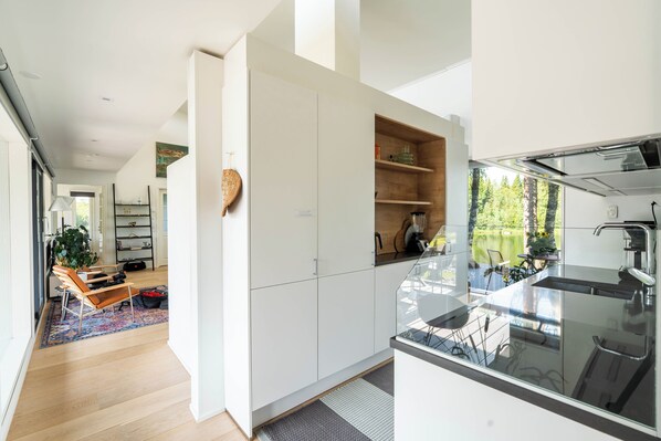 A modern kitchen with white cabinets, a built-in oven, and a large window overlooking a garden. - The Iconic Wikkelä Villa (Ranua)