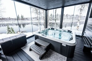 Un jacuzzi en una terraza con vistas a un lago helado y árboles.