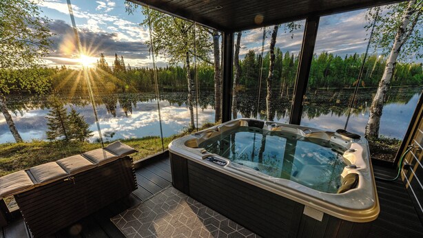 Een hottub op een terras met uitzicht op een meer en bomen.